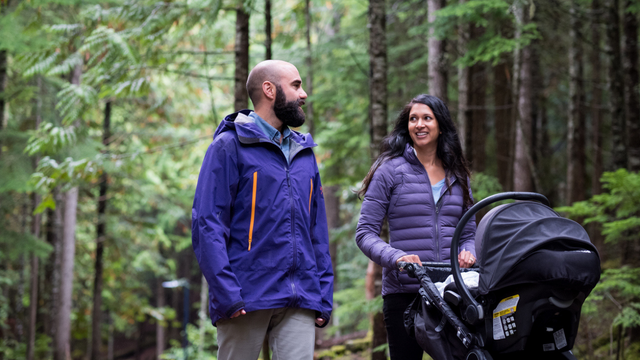 A couple walks in the woods with baby in stroller